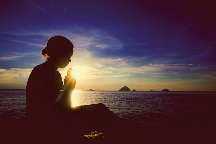 49180882 - young woman praying sunset over the ocean concept